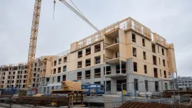 En byggkran står intill ett flerbostadshus med ofärdig fasad.