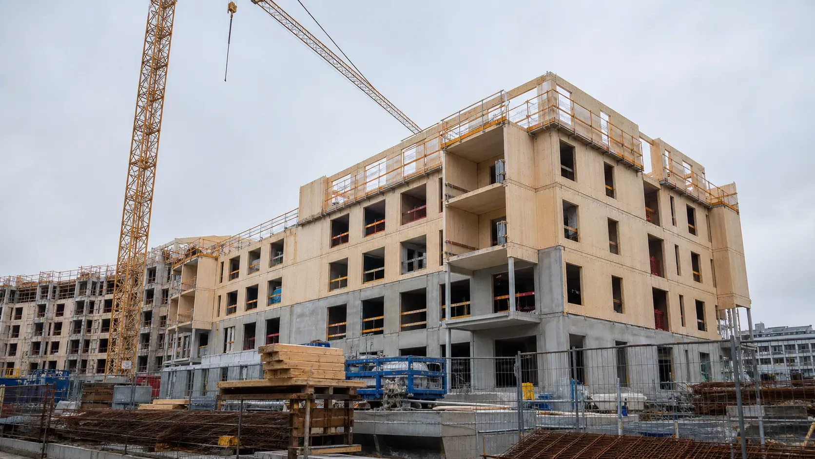 En byggkran står intill ett flerbostadshus med ofärdig fasad.