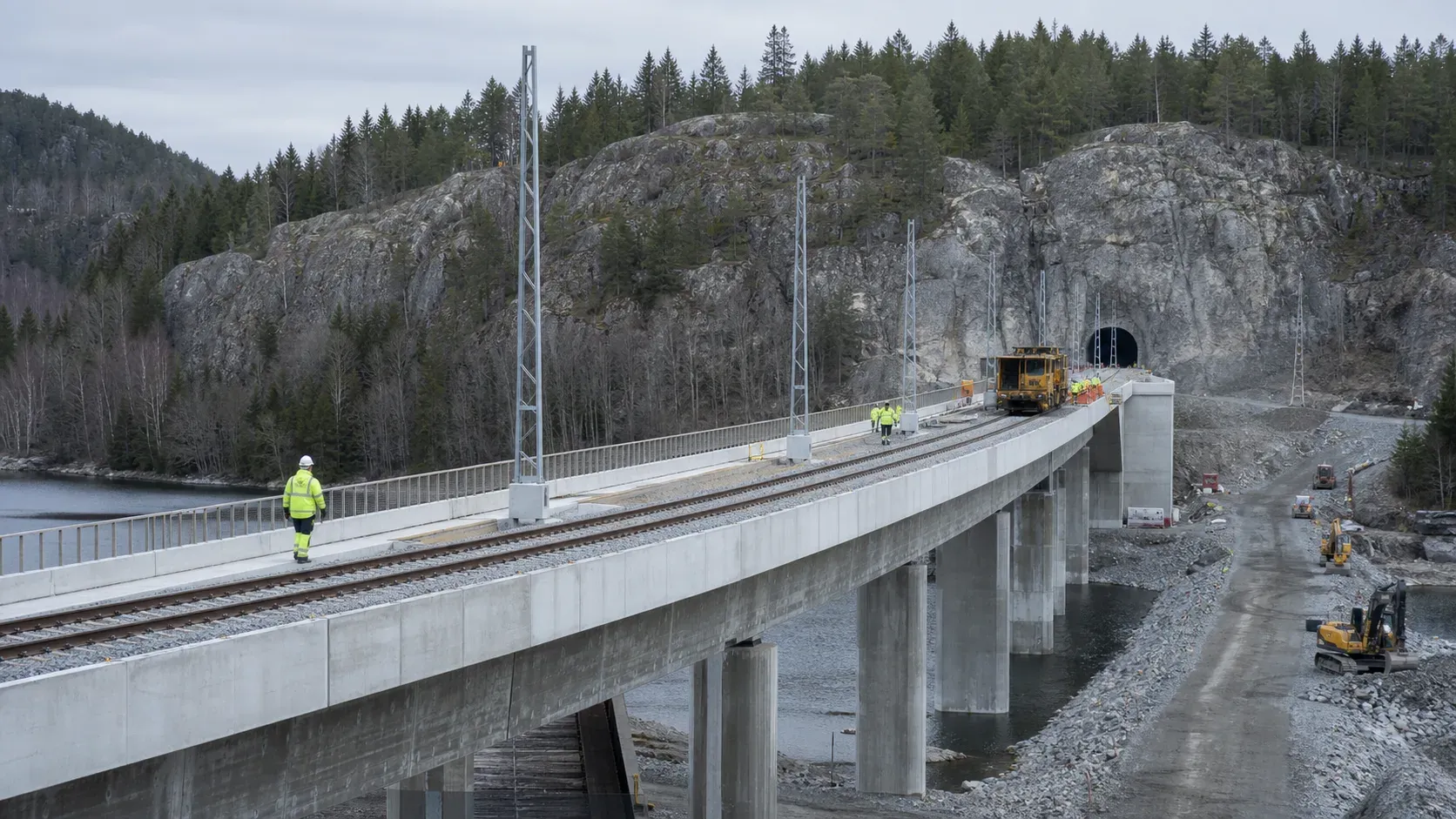 En järnvägsbro under arbete leder mot en tunnel genom berget.