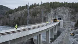 En järnvägsbro under arbete leder mot en tunnel genom berget.