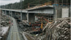 Järnvägsspår går genom en byggarbetsplats under en bro.