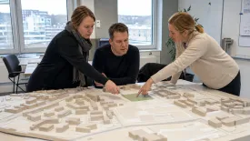 Tre personer pekar ut delar av ett kvarter i en stadsmodell.